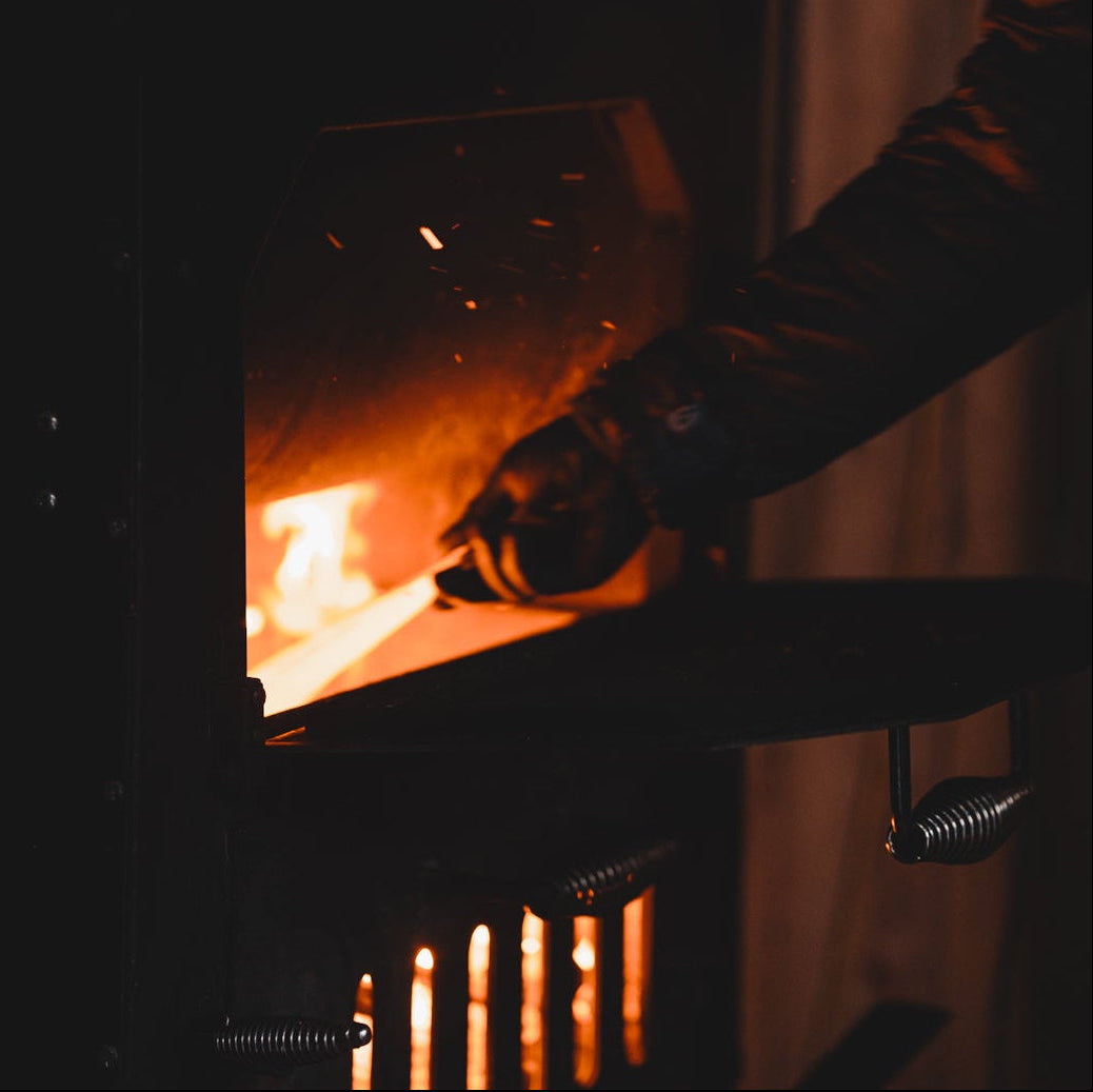Person lighting a fire in a wood stove with a warm glow