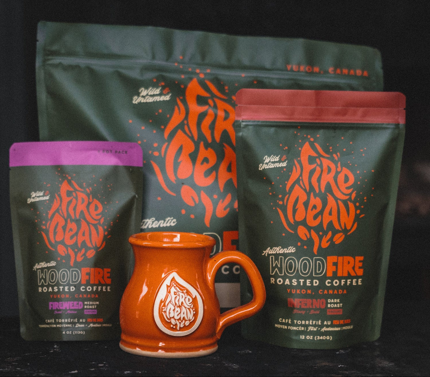 Three packages of 'Fire Bean' coffee and an orange mug on a dark background