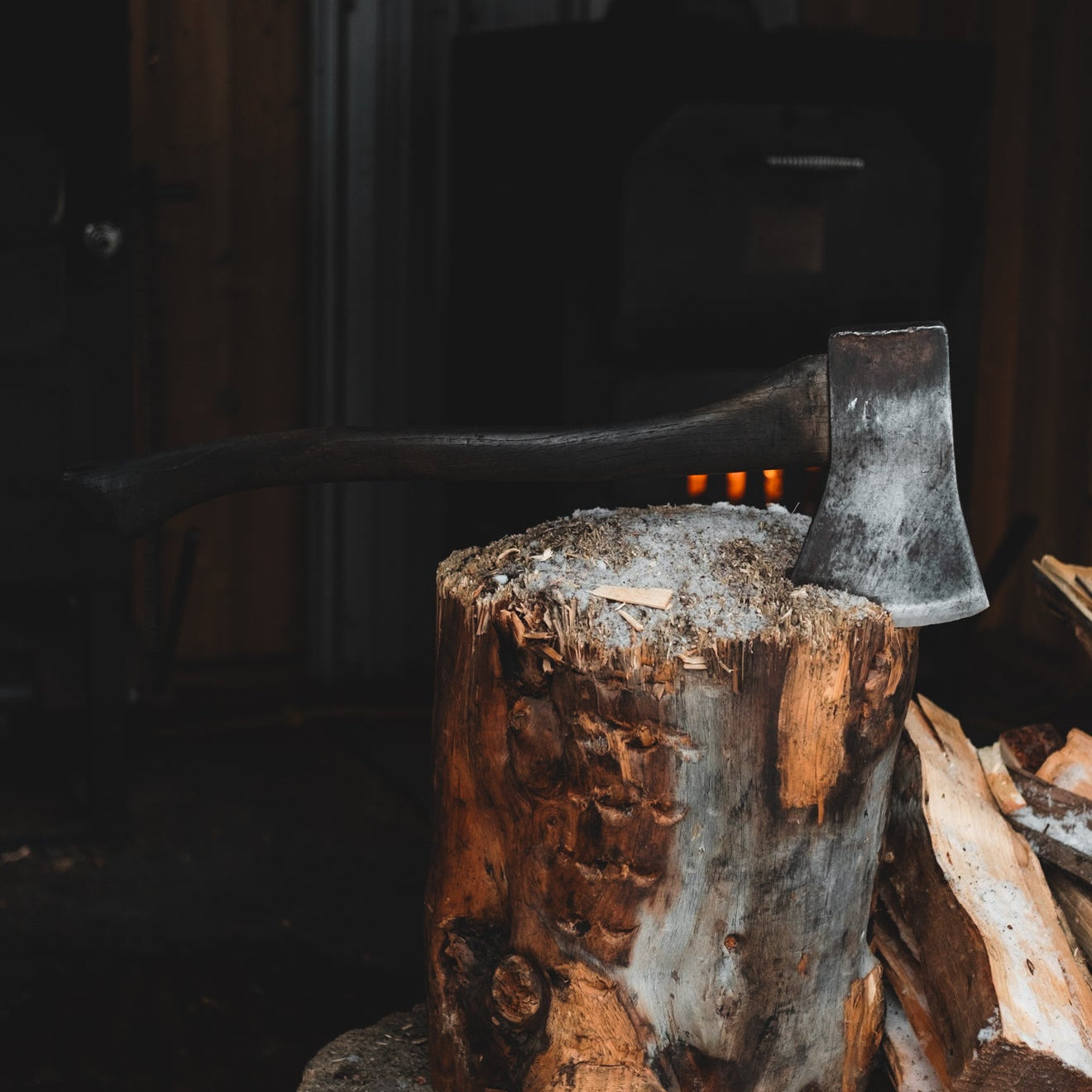 Wooden stump with a axe and stacked firewood in a dimly lit room