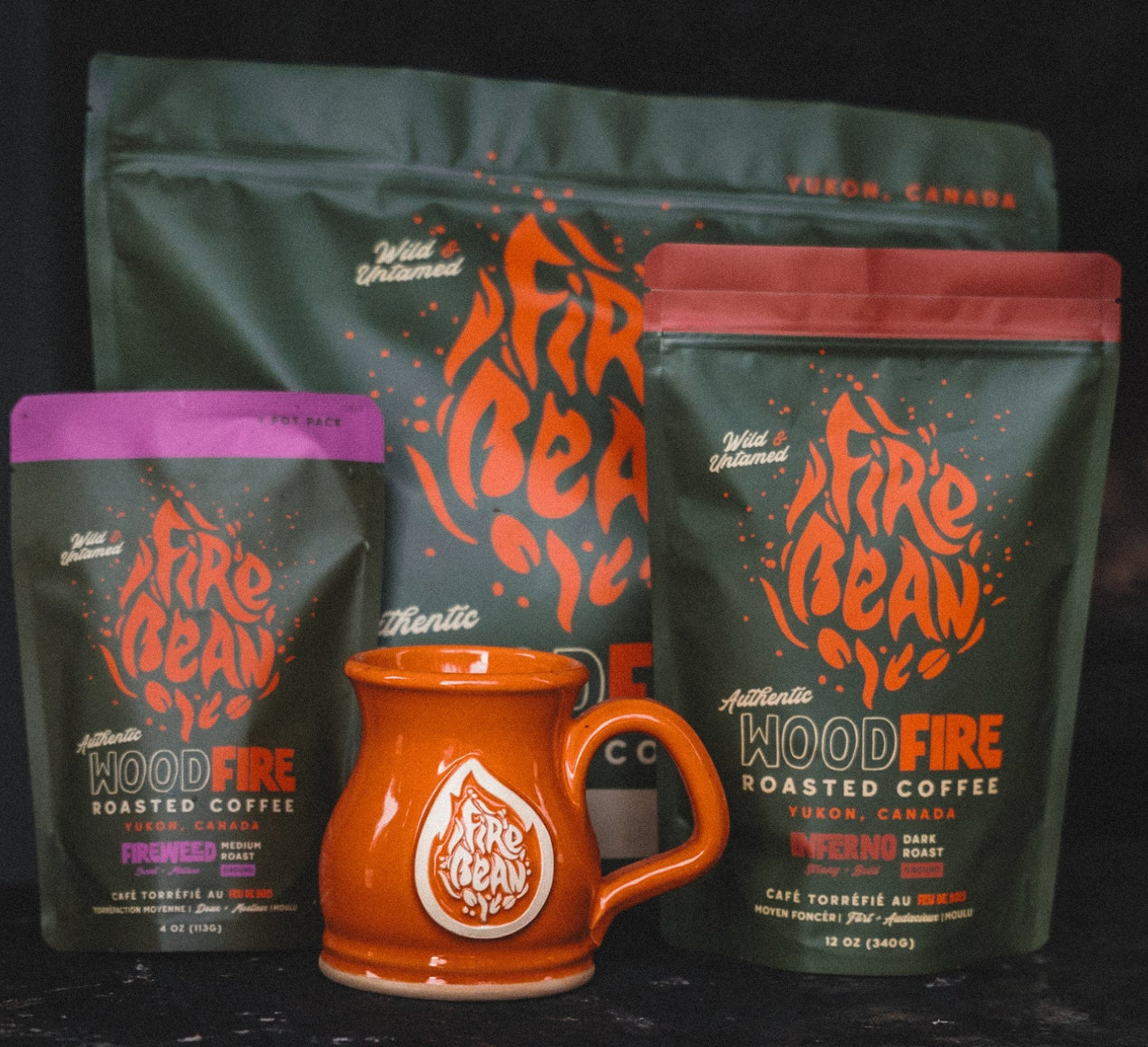 Three packages of 'Fire Bean' coffee and an orange mug on a dark background