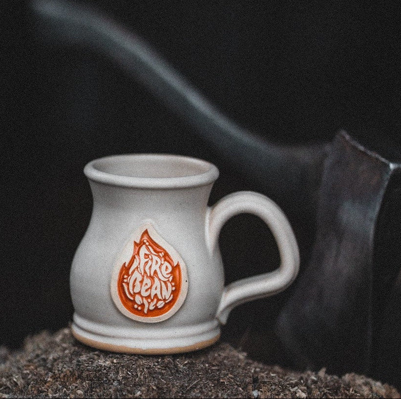 White mug with a logo on a wooden stump in front of a blurred fire