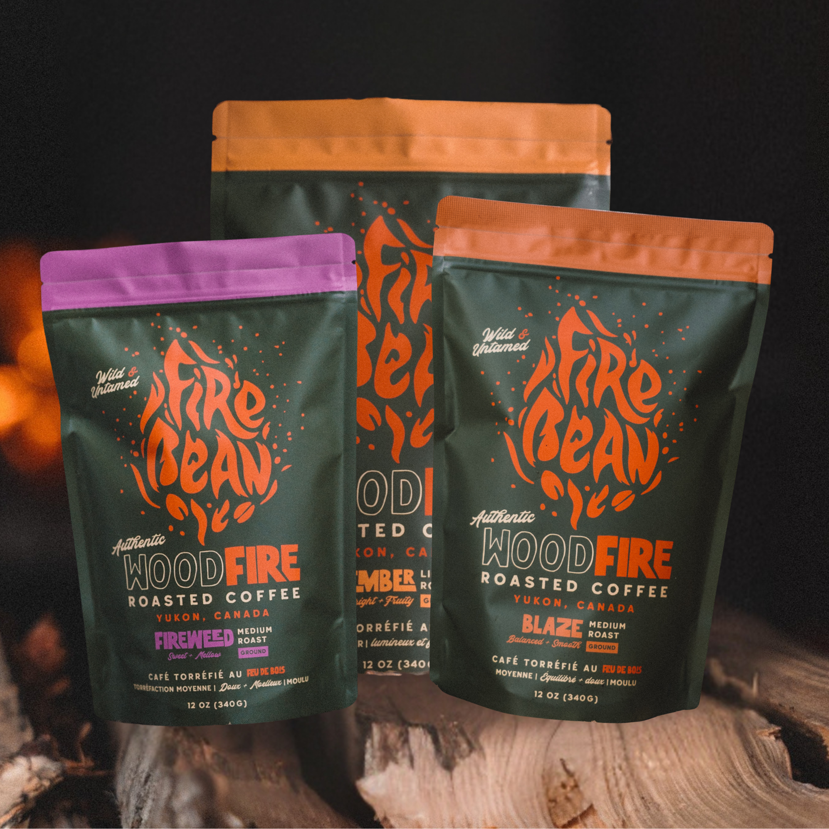 Three packages of Fire Bean WoodFire roasted coffee on a dark background with a fire.